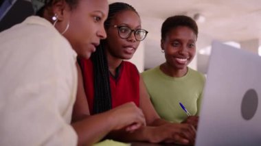 Üç genç Afrikalı Amerikalı kız öğrenci laptopta çalışarak ve fikirlerini paylaşarak bir araya geldiler. Nesiller z arkadaşları üniversite projesinden bahseden siyah kadınlar, kapalı alandaki bilgisayarları kullanıyorlar ve izliyorlar.