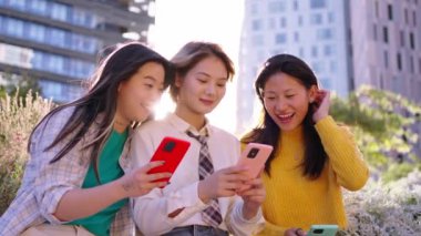 Akıllı telefon kullanarak cep telefonundan komik videolar izlemekten mutlu gülümseyen üç genç Asyalı kadın grubu. Jenerasyon z Çinli bayan arkadaşlar birlikte neşeli görünürler kapalı mekanda