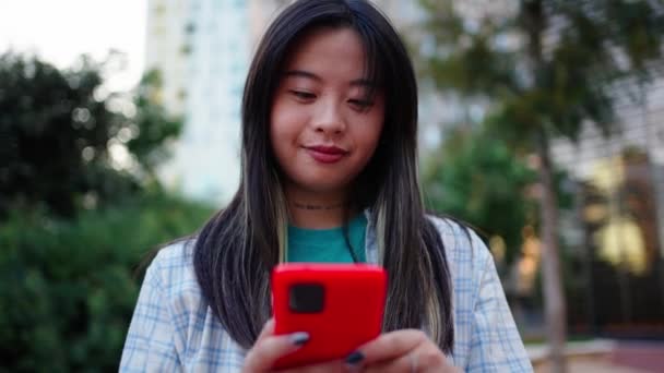 在城市街道上 快乐的亚洲年轻女子用手机笑着 在社交媒体上欣赏视频内容的时候 一代漂亮的中国女性看上去很高兴 网络成瘾者 — 图库视频影像
