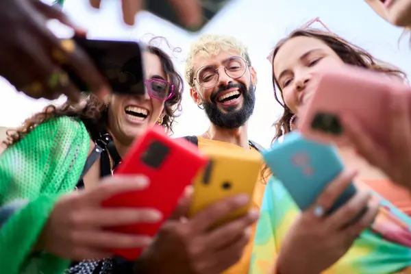 A group of happy people is celebrating and sharing a fun moment using mobile with their colorful cell phones, smiling and making gestures. Youth people o millennial generation addicted to technology