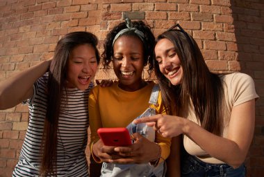 Üç kadın bir şişe alkollü içeceği bir cep telefonuna bakıp birlikte geçirdikleri eğlenceli ve boş zamanlarının fotoğrafını çekerken mutlu bir şekilde paylaşıyorlar.