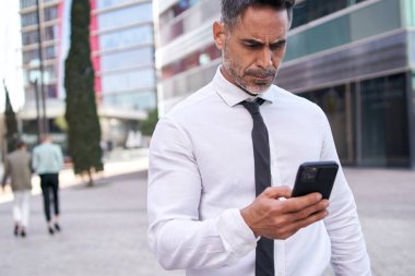 Yakışıklı, gri saçlı iş adamı ofis binasının önünde duruyor. Geçmişi bulanık, fotokopi alanı var. Olgun erkek profesyonel mola yerinde cep telefonunu kullanıyor. 