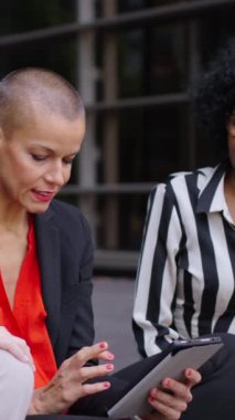 Çok kültürlü yetişkin iş kadınlarından oluşan dikey bir grup ofis binasının dışında sessizce sohbet ediyorlar. Profesyonel kadınlar açık havada tablet bilgisayar kullanarak ve arayarak pazarlama stratejisinden bahsediyorlar.