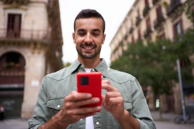 Genç beyaz adam Avrupa 'nın Barselona şehrinde caddede mutlu bir cep telefonu arıyor. Hücre kullanan neşeli erkek turist, dışarıda seyahat deneyiminin eğlenceli atmosferinin tadını çıkarıyor
