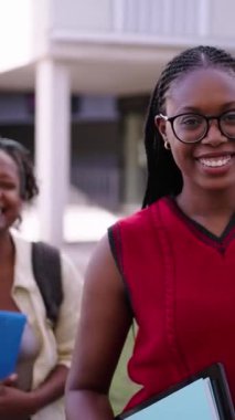 Dikey portre gülümsüyor ve neşeli genç bayan sınıf arkadaşları birbirlerine yaslanıyor ve kameraya bakıyor. Üçüncü grup Afro-Amerikan bayan arkadaşları ellerinde video dosyaları için poz veriyorlar.