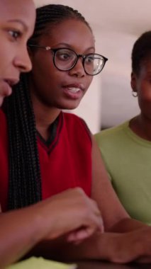 Dikey olarak üç genç Afrikalı kız öğrenci çalışarak ve fikirlerini paylaşarak bir araya geldiler. Nesiller boyunca siyahi kadınlar bir araya gelip üniversite projesini konuşuyor, bilgisayarları kullanıyor ve ev içi bilgisayarlara bakıyor.