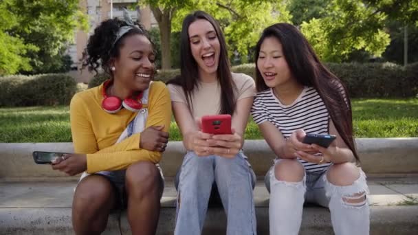 Tre Gioiose Donne Multirazziali Che Usano Telefono Seduto All Aperto — Video Stock