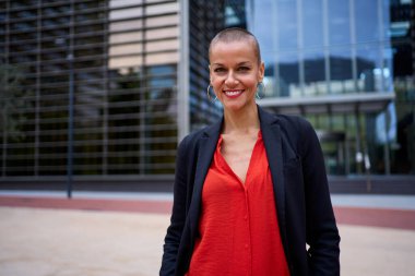 Kurumsal ofis alanında şık kırmızı giyinmiş modern Kafkas iş kadını. Güçlü ve güçlü, kısa saçlı, gülümseyen ve dışarıda kameraya mutlu bakan bir kadın. Boşluğu kopyala