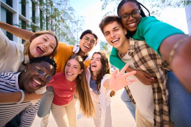 Çok ırklı bir grup genç, selfie çekerken ön kameraya bakıp gülüyor ve dışarıda birlikte eğleniyorlar. Genç öğrenciler sokak şehrindeki arkadaşlarıyla boş zamanlarının tadını çıkarıyorlar.