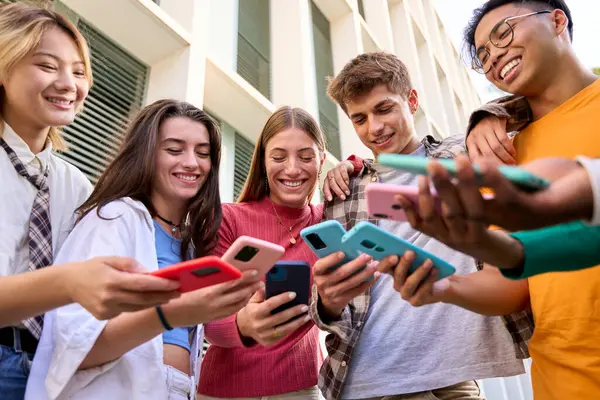 Group of multiracial generation z young smile happily watching funny videos on a smart phone they holding in their hands. Friends having fun together using social video game on mobile cell outdoor