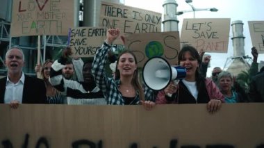 İklim değişikliğini protesto eden bir grup gösterici. Yürüyüşte çeşitli insanlar çevre lehinde pankartlarla bağırıyor.