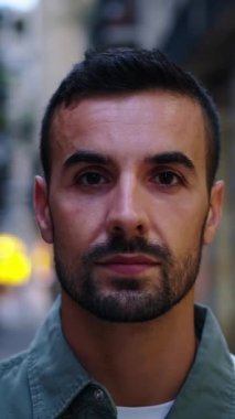 Dikey kamera zumlayan genç sakallı yakışıklı adam Avrupa 'nın Barcelona şehrindeki caddede ciddi bir şekilde kameraya bakıyor. Kafkasyalı erkek turist açık hava gece turizmi için ciddi poz veriyor.