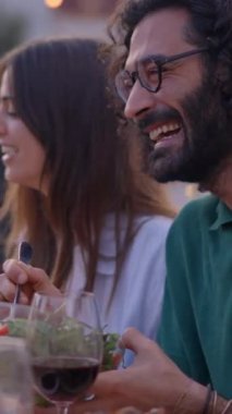 Dikey. Gülümseyen insanlar arkadaşlarıyla mangal ve içecek buluşmalarında eğleniyorlar. Gün batımında terasta yiyip içen çift. Çok ırklı bir grup gülen arkadaş yemeği kutluyorlar.