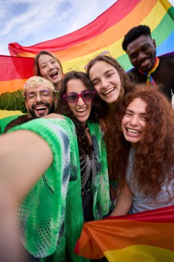 Gökkuşağı bayrağıyla dikey selfie çektirmek için renkli tebessümlü mutlu insanlardan oluşan bir kalabalık onların eğlencesini ve eğlencelerini yakalıyor. Gay ve lezbiyen arkadaşlar LGBT 'nin gay onur yürüyüşü konseptinde birlikteler