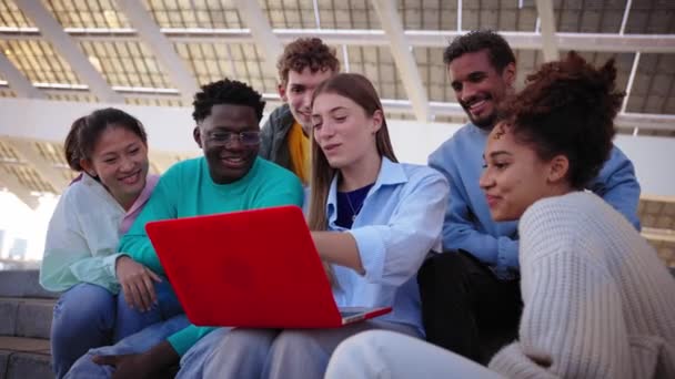 一群快乐的年轻人静静地坐在楼梯上 用他们的手机用笔记本电脑笑着 笑着谈论学习任务 — 图库视频影像