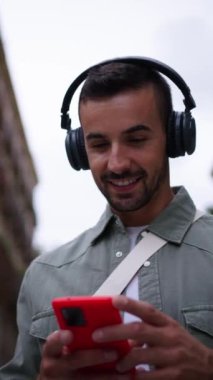 Dikey, genç ve çekici bir adam kulaklık takıyor ve Avrupa 'da sokakta müzik dinlemekten hoşlanıyor. Kırmızı hücre turizmini kullanarak gezen mutlu erkek turist.
