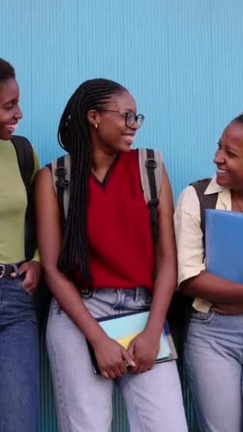 縦の3人の笑顔の黒人女性学生が お互いに喜んで見つめ合うフォルダを抱えていました 幸せな若い遺伝子の友人アフリカの素敵な女性は ブルーウォールの孤立した背景にリークバックパック — ストック動画