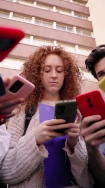 Dikey alçak açı. Bir grup genç ve ciddi insan cep telefonlarını birlikte kullanıyor. Yoğunlaşmış arkadaşlar sosyal medyadan içeriği izlemek için mobil ekranda toplandılar. Gen Z teknolojisi bağımlısı