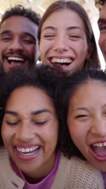 Dikey. Bir grup gülen çoklu etnik gruptan insan akıllı telefonlarının ön kamerasına bakarak birlikte fotoğraf çekiyorlar. Z neslinin çeşitli arkadaşları dışarıda eğleniyor.