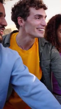 Dikey. Bir grup çok ırklı genç insan gülümsüyor, el ele tutuşuyor ve onları bir takım jesti ile havaya kaldırıyor, özel bir etkinliği kutluyor ve birlikte olmanın ve açık havada arkadaşlığın tadını çıkarıyorlar.