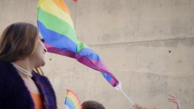 LGBT gökkuşağı bir duvarın önünde rüzgarda sallanıyor. El ele tutuşan gay gurur bayrağı. Çeşitli insanlar dans ediyor ve bayrak altında eğleniyor. Lezbiyen, gey, biseksüel, homoseksüel, transseksüel sosyal hareketler