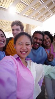 Bir grup çok ırklı genç arkadaşı olan Çinli bir kız akıllı telefonun kamerasına bakarak dikey selfie çekerek mutlu bir anı paylaşıyor. Gülümseyen insanlar eğleniyor. Hafta sonu tatili