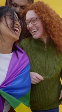 Dikey. Dansçılar ve heyecanlı genç LGBT 'liler gülerek gay onur günü festivalinin tadını çıkarıyorlar. Bir grup neşeli arkadaş, gökkuşağı bayraklı sarı bir duvarın önünde birlikte eğleniyorlar. 