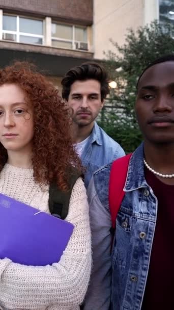 垂直的 一群严肃而自信的多种族学生站在那里 拿着文件夹和背包看着大学校园里的摄像机 同学们聚集在大学外面 — 图库视频影像