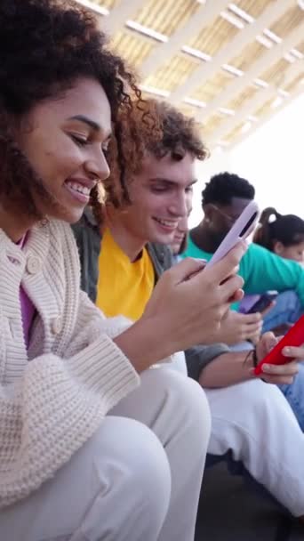 垂直的 快乐的年轻人正静静地坐在楼梯上 一边用手机微笑 一边分享有趣的视频 他们似乎在户外玩得很开心 技术成瘾的一代 — 图库视频影像