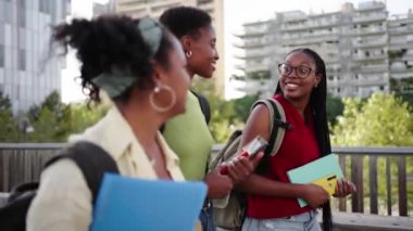 Üç Afro-Amerikalı kız öğrenci üniversite kampüsünde kaygısızca dolaşıyorlar. Genç siyah bayan arkadaşlar, açık havada güneşli bir gün için sırt çantaları ve çalışma kitaplarıyla mutlu mesut yürürler.