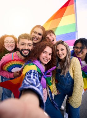 Dikey eğlenceli selfie LGBT grubu genç arkadaşları ellerinde gökkuşağı bayrağı tutarak gey onur gününü kutluyorlar. Homoseksüel insanlar topluluğu gülümsüyor ve açık havada resim çekiyor. z pozitif ilişkileri oluşturma.