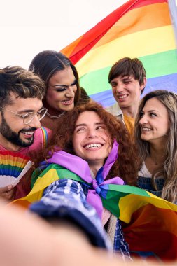 Dikey. Eğlenceli selfie LGBT grubu genç arkadaşları ellerinde gökkuşağı bayrağı tutarak eşcinsellerin gurur gününü kutluyor. İnsanlar gülümsüyor ve dışarıda neşeli bir resim çekiyor. z pozitif ilişkileri oluşturma.