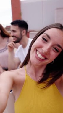 Heyecanlı genç bayan çatıda sosyal medya için selfie dikey videosu kaydediyor. Neşeli kadın dışarıda kameralara farklı arkadaşlarla yüz ifadeleri takınırken komik görünüyor. İnsanlar kutlama için toplandı