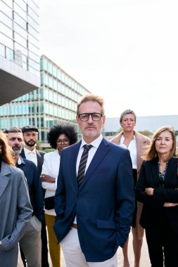 İş yerinin önünde kendine güvenen ve ciddi görünen farklı iş adamlarından oluşan bir ekibin dikey videosu toplandı. Lider bir adım öne çıkar ve kendini patron olarak gösterir.