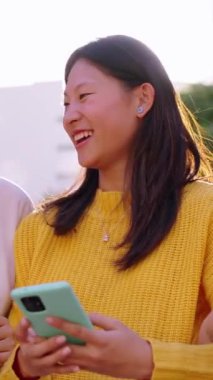 Dikey neşeli Asyalı bayan arkadaşlar gülen cep telefonu arayarak yürürler. Genç Çinli kızlar güneşli bir günde cep telefonlarını kullanarak birlikte dolaşmaktan hoşlanırlar. Pozitif sosyal ilişkiler nesli z 