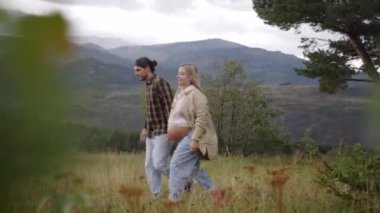 Kırsalda yürüyen hamile, beyaz bir çift. Mutlu insanlar bir sonbahar günü dağlarda el ele yürüyorlar. Nişanlı partner dışarıda eğleniyor..