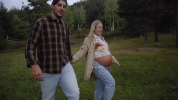 妊娠中の女性と男性がマウンテンパークでリラックス 両親の若いカップルは ハッピーな手で屋外を歩いています 妊娠3年目の家族ロマンチックなヘルスケアコンセプト — ストック動画