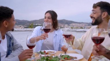 Barbekü partisini çatıda kutlayan genç arkadaşlarımızın şerefine. Gülümseyen insanlar kadeh kaldırıyor ve kırmızı şarap içiyor. Sağlıklı yiyecekler yiyorlar. Açık havada bir bahar gününün tadını çıkarıyorlar.