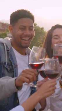 Dikey. Bir grup çok ırklı arkadaş kırmızı şarap içip kutlama partisi yapıyorlar. Gülen gençler kucaklaşıp dışarıda eğleniyorlar. Erkekler ve kızlar yaz tatilinin tadını çıkarıyorlar..