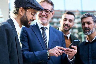 Neşeli bir grup Kafkasyalı iş adamı patronun cep telefonuna bakmak için toplandı, işe ara verdiler. Mobil video ekranda profesyonel erkek saati olarak ifadeleri ve tepkileri birlikte yakalar