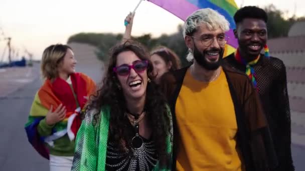 Lgbtの人々のグループは カラフルな虹の旗を掲げるゲイのプライドデーパレードで 楽しい 友情と幸せなイベントを楽しんで通りをゆったり歩いています 多様な男性と女性が一緒に走る — ストック動画