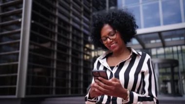 Yetişkin Afro-Amerikan iş kadını resmi takım elbiseli bir ofis binasının önünde cep telefonu kullanarak duruyor. Son sınıf öğrencisi Latin bir bayan hücresinde yazarken gülüyor ve heyecanlanıyor.