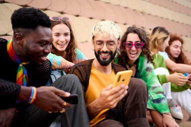 Bir grup farklı insan ellerinde cep telefonlarıyla dışarıda gün boyu eğleniyor. Cep telefonu kullanan çok ırklı genç arkadaşlar. Güzel milenyum, birlikte oturmuş üniversite tatilinde heyecanla gülüyoruz..