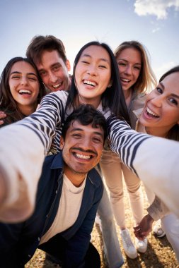 Bir grup mutlu genç arkadaş kameraya gülümseyen bir şekilde birlikte dikey selfie çekiyorlar. Milenyum insanları sırtına poz vererek neşeli anları paylaşıyorlar. Dostluk ve toplum