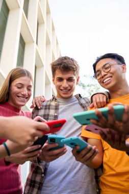 Çok ırklı, genç ve neşeli insanların ellerinde akıllı bir telefonla eğlenceli video oyunları oynadığı dikey bir grup. Arkadaşlar dışarıda cep telefonlarını kullanarak eğleniyorlar.