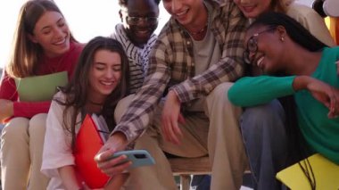 Çok ırklı bir grup genç, selfie çekerken ön kameraya bakıp gülüyor ve dışarıda birlikte eğleniyorlar. Genç öğrenciler sokak şehrindeki arkadaşlarıyla boş zamanlarının tadını çıkarıyorlar.