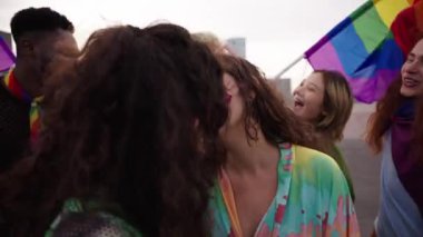 Eşcinsel gururu festivalinde öpüşen iki genç kız. Igbt partisini arka planda gökkuşağı bayrağı ve hayranlarıyla kutlayan bir grup arkadaş. Z nesli ve cinsellik türleri.