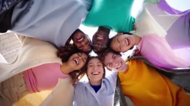 Renkli tişörtler giymiş, gülümseyen ve birbirlerine sarılan bir grup çok ırklı genç arkadaşın alçak açısı. İnsanlar birbirini kucaklıyor, eğleniyor ve arkadaşlığın tadını çıkarıyor.