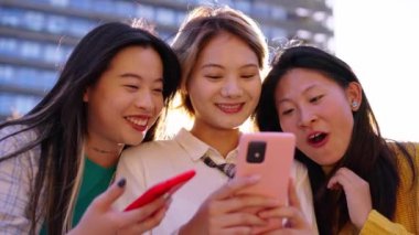 Üç kuşak güzel Çinli kadın cep telefonundan komik videolar izlerken mutlu bir şekilde gülüyor. Genç ve güzel Asyalı bayan arkadaşlar birlikte oturup güneşli günün tadını çıkarıyorlar. Dışarıdaki hücreleri neşeli görünüyor.