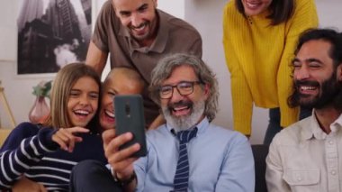 Kafkasyalı çok nesilli aile oturma odasında cep telefonu kullanarak kanepede toplandı. Mutlu insanlar eğlenceli bir ifadeyle gülümsüyor. Hücrede eğlenceli videolar izleyip eğleniyorlar.